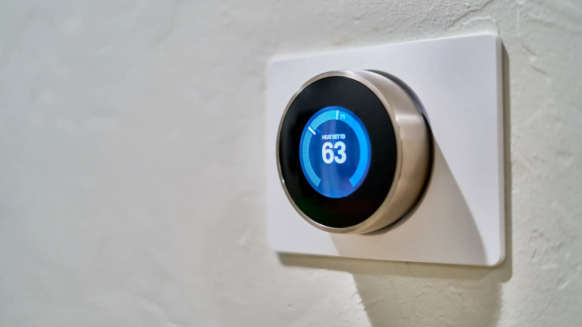 A smart thermostat against a white wall backdrop.